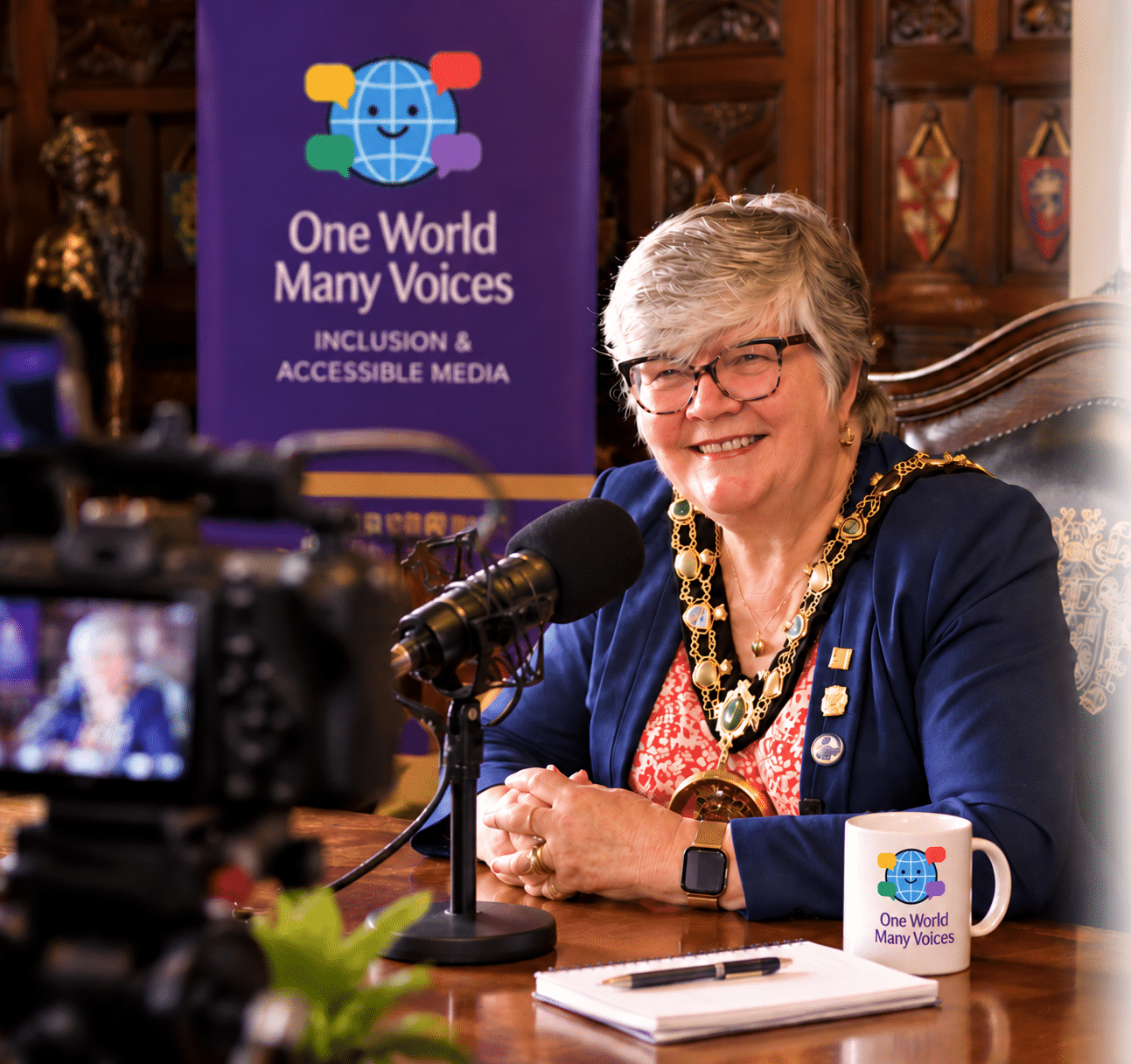 AI-enhanced illustration of an OWMV mayoral podcast interview, with the Mayor, microphone, video camera and official OWMV logos on the banner and mug.